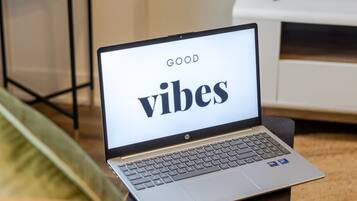 A laptop on a table displaying 'GOOD vibes' with a TV in the background.