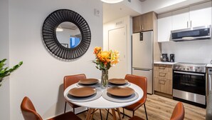Une cuisine moderne dotée d’appareils électroménagers en acier inoxydable, un coin repas avec une table ronde et des chaises, et un miroir décoratif sur le mur.