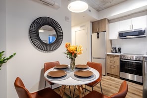 A modern kitchen with stainless steel appliances, a dining area with a round table and chairs, and a decorative mirror on the wall.