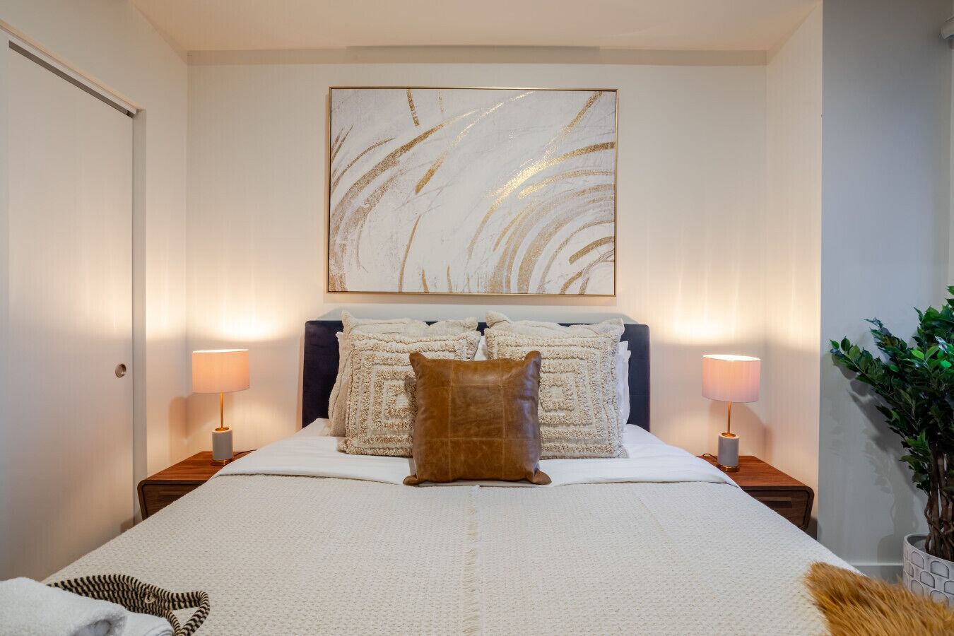 Een netjes ingerichte slaapkamer met een groot bed, twee bedlampjes, een decoratief hoofdeinde en een kunstwerk aan de muur.