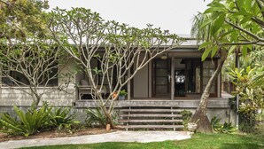 A modern house with a stone facade, a wooden deck, and a well-maintained garden with various plants and a tree.