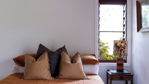 A bedroom with a bed, pillows, a nightstand, a lamp, and a window with a view of trees.