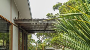 A wooden deck with a table and chairs, surrounded by lush greenery and trees.