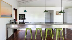 A modern kitchen with a stainless steel island, green bar stools, and pendant lighting.