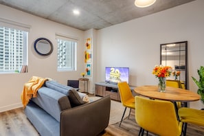 Una sala de estar moderna con un sofá, una mesa de comedor con sillas, un televisor y obras de arte en las paredes.