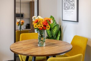 A round wooden table with a vase of flowers, yellow chairs, and a framed artwork on the wall. - Modern 1-BDR APT in DT MTL – Prime Location! (Montréal)
