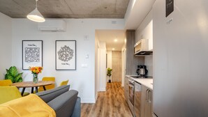 Une cuisine moderne dotée d’appareils électroménagers en acier inoxydable, un coin repas avec un canapé et des chaises jaunes, et des œuvres d’art accrochées aux murs.