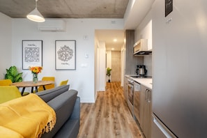 Una cocina moderna con electrodomésticos de acero inoxidable, un comedor con sofá y sillas amarillas, y obras de arte en las paredes.