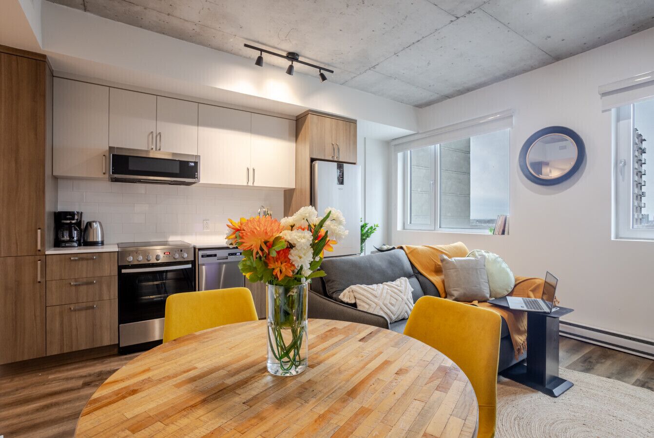Een moderne keuken met inbouwapparatuur, een eettafel met stoelen, en een zithoek met een bank en een laptop op een standaard.