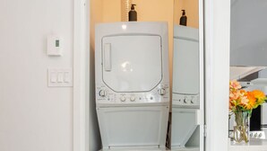 A laundry room with a washing machine and dryer, a thermostat, and a small shelf with a bottle.
