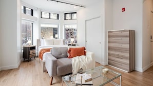 A modern bedroom with a sofa, a glass coffee table, a dresser, and large windows.