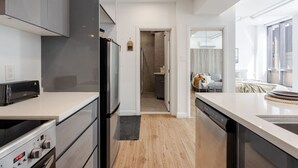 Una cocina moderna con horno empotrado, microondas y lavavajillas. Tiene piso de madera y vista al área de estar contigua.