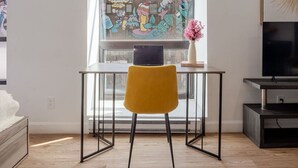 Una sala de estar moderna con un ventanal grande, un sillón amarillo, una mesita y un televisor sobre un mueble.