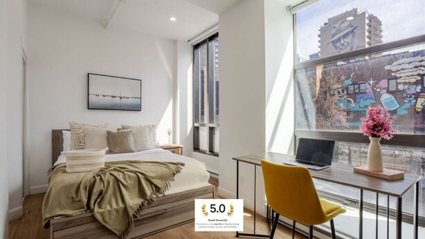 Un dormitorio moderno con cama, escritorio y ventana con vista a la ciudad.