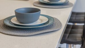 Una cocina con una encimera larga, dos cuencos sobre platos a juego, un lavabo y un piano al fondo.