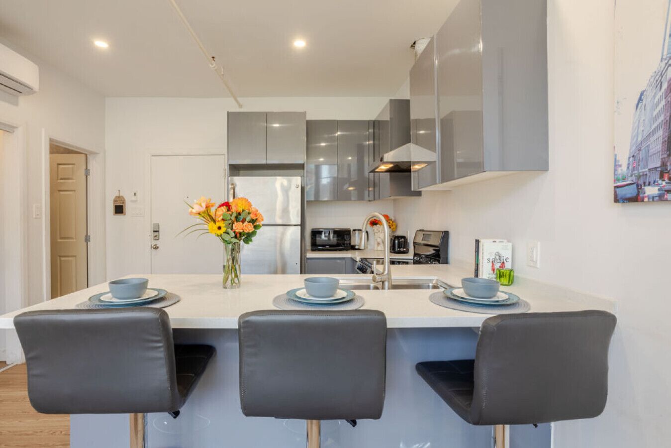 Une cuisine moderne dotée d’un îlot central, de meubles gris, d’appareils électroménagers en acier inoxydable et d’un coin repas avec trois chaises grises.