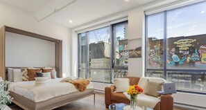 A modern bedroom with a bed, a sofa, a coffee table, and large windows. - MTL Urban Apartment – Prime Downtown Spot (Montréal)