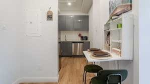 Una cocina moderna con armarios grises, un lavavajillas de acero inoxidable y una encimera blanca. Hay una mesa pequeña con dos platos y un jarrón con flores.