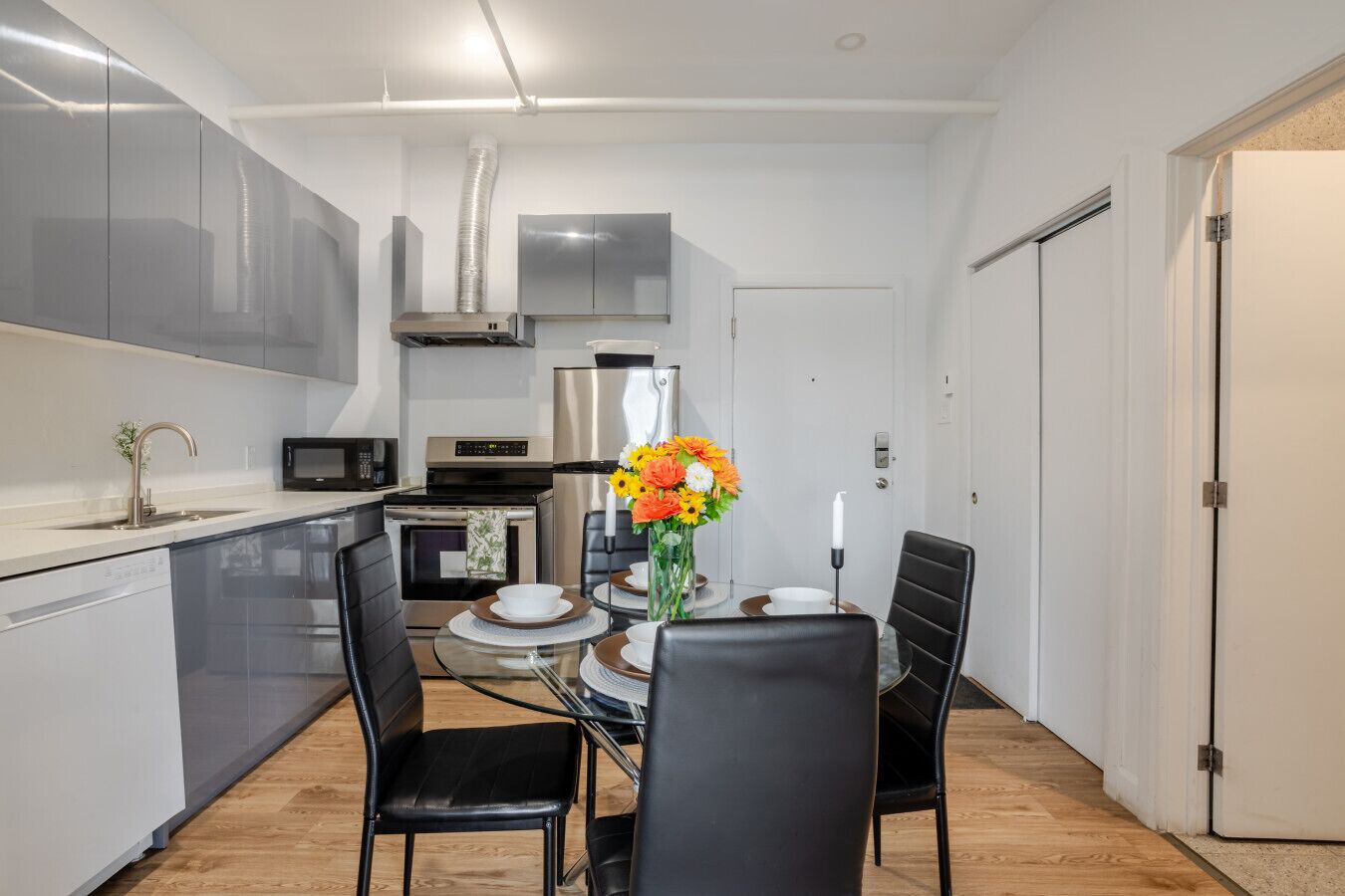 Una cocina compacta con electrodomésticos modernos, una mesa de comedor con sillas y un pequeño florero decorativo.