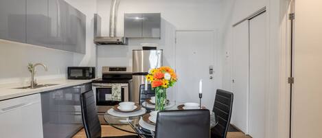 Una cocina compacta con electrodomésticos modernos, una mesa de comedor con sillas y un pequeño florero decorativo.