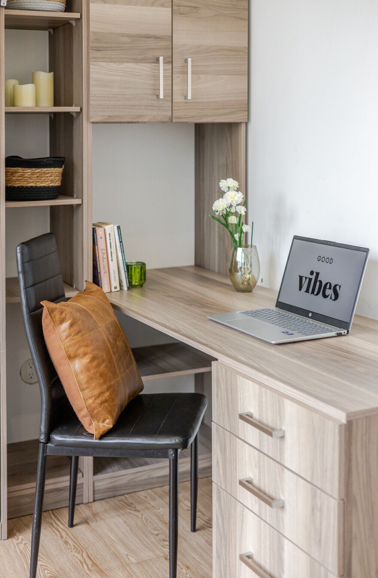 A workspace with a laptop, a chair, a desk, a bookshelf, and a vase with flowers.