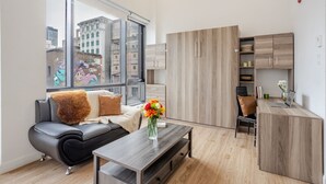 Un salon moderne avec un canapé, une table basse et une vue sur le paysage urbain, visible à travers de grandes fenêtres.