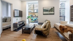 Un salon moderne avec un canapé, une table basse, un téléviseur et une vue sur le paysage urbain grâce à de grandes fenêtres.