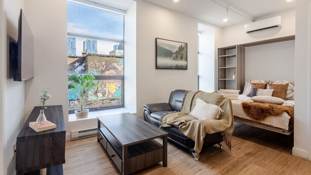 Un salon moderne avec un canapé, une table basse et une vue sur les immeubles à travers une grande fenêtre.