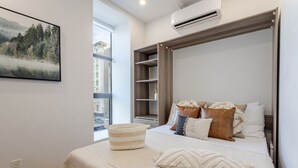 Une chambre avec un grand lit, une fenêtre, une étagère intégrée et un appareil de climatisation.