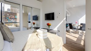 A modern hotel room with a bed, a TV, a dining area, and a balcony.