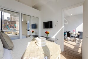 A modern hotel room with a bed, a TV, a dining area, and a balcony.