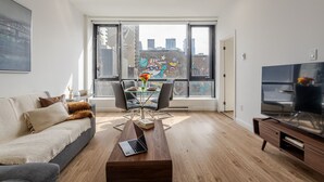 A modern living room with a sofa, coffee table, TV, and a dining area with chairs and a table.