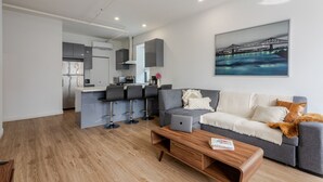 A modern living room with a grey sofa, a coffee table, and a kitchen area in the background.