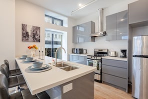 A modern kitchen with a central island, stainless steel appliances, and a large window providing natural light.