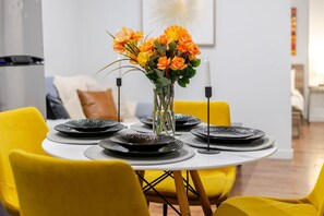 Une table à manger avec des assiettes noires, un vase rempli de fleurs oranges et des chaises jaunes.