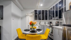 A modern kitchen with a dining area, featuring a round table with yellow chairs, a vase with flowers, and stainless steel appliances. - Charming 1BDR – Prime Location on Bishop St (Montréal)