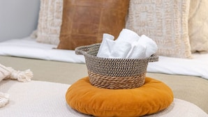 A bed with a woven basket containing white towels, a mustard-colored pillow, and a white throw blanket. - Charming 1BDR – Prime Location on Bishop St (Montréal)