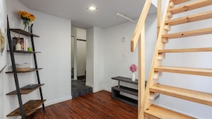 Ein Zimmer mit einer Holztreppe, einem dunklen Holzboden, einer weißen Wand und einem kleinen Holztisch mit einem Blumenstrauß.