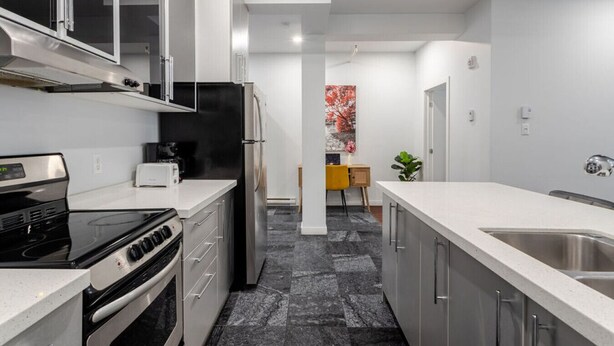 A modern kitchen with stainless steel appliances, a central island, and a view into the dining area. - Vibrant MTL Living – 1BDR in a Top Location (Montréal)