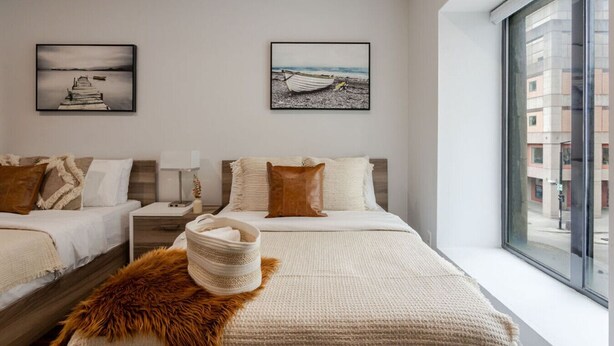 A modern hotel room with two beds, a large window with a city view, and artwork on the walls. - Vibrant MTL Living – 1BDR in a Top Location (Montréal)