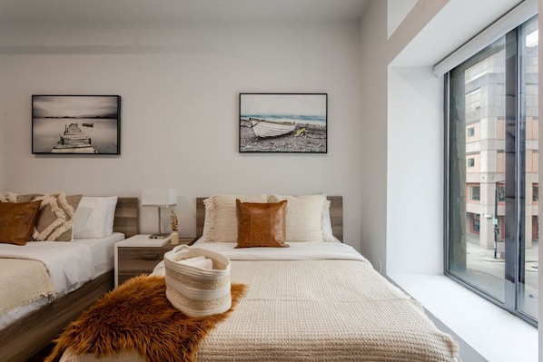 Ein modernes Hotelzimmer mit zwei Betten, einem großen Fenster und Stadtblick sowie Kunstwerken an den Wänden.