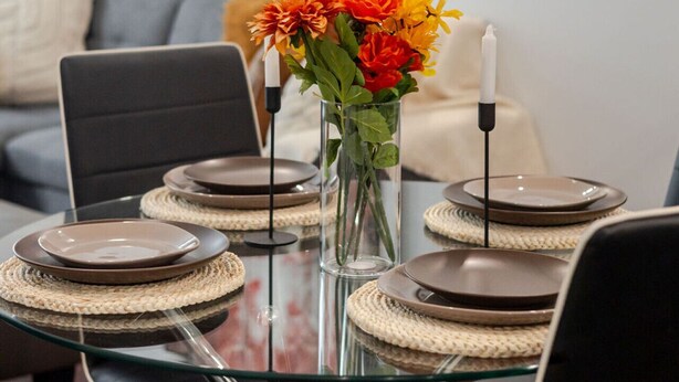 A dining area with a glass table, plates, and a vase of flowers. - Vibrant MTL Living – 1BDR in a Top Location (Montréal)