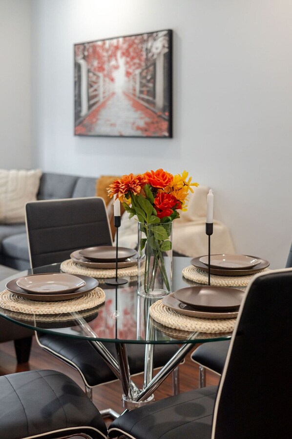 Un coin repas avec une table en verre, des assiettes et un vase de fleurs.