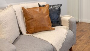 A grey sofa with a beige throw blanket and two pillows, one brown and one dark grey. - Spacious Bishop Apartment –Prime Downtown Stay (Montréal)