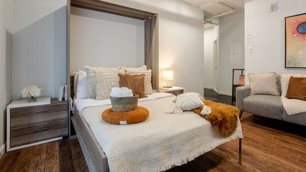 A modern bedroom with a large bed, a side table, a grey sofa, and a painting on the wall. - Spacious Bishop Apartment –Prime Downtown Stay (Montréal)