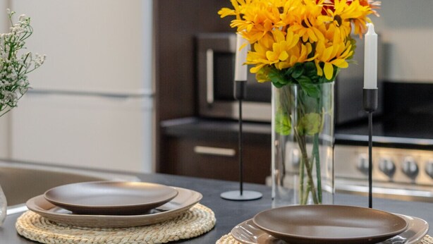 Una encimera de cocina con un jarrón de flores amarillas, dos platos y un mantel tejido.