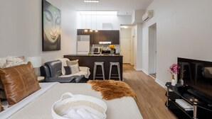 Una sala de estar moderna con sofá, mesa de centro, televisor y área de cocina con refrigerador, microondas y taburetes de bar.