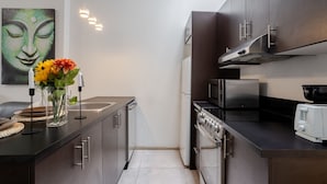 Una cocina moderna con electrodomésticos de acero inoxidable, una encimera oscura y un florero con flores.