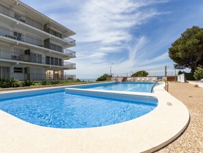 A swimming pool with a clear blue water, surrounded by a sandy area and a building with multiple balconies. - Apartment Ulises by Interhome (Salou)