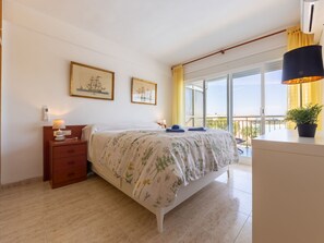 A bedroom with a bed, bedside table, lamp, and a window with curtains. - Apartment Ulises by Interhome (Salou)